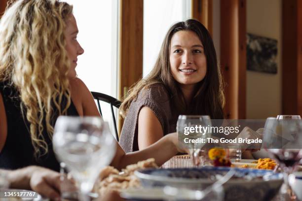 young woman talking while sitting by sister at dining table during thanksgiving - heritage celebration inside stockfoto's en -beelden