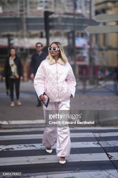 Candela Novembre wears sunglasses, earrings, a pale pink oversized puffer jacket from Miu Miu, matching pale pink large cargo pants from Miu Miu,...