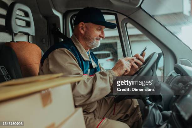 delivery man checking order on cellphone - delivery truck stock pictures, royalty-free photos & images