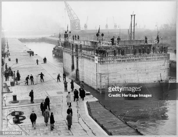 View of the cooling water intake caisson for Coryton Oil Refinery leaving the lock at Tilbury Docks, with people on the side of the lock using ropes...