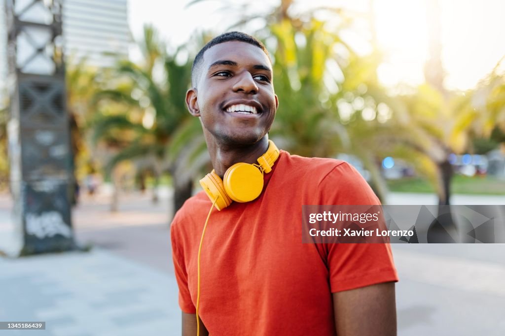 Happy man with headphones standing in the street while looking away