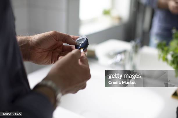 midsection of man checking blood sugar through glaucometer in bathroom - glaucometer stockfoto's en -beelden