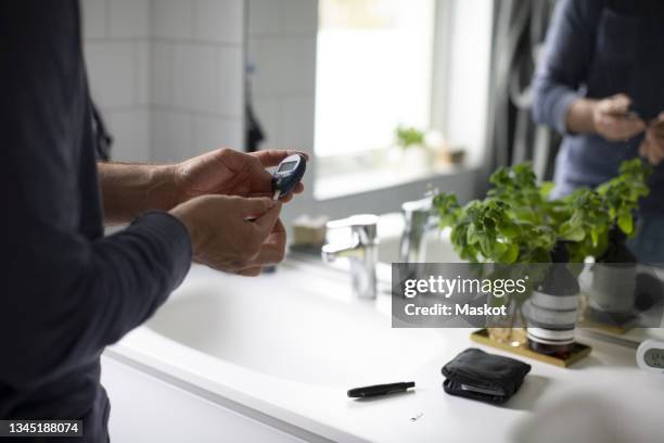 mature man checking diabetes through glaucometer in bathroom at home - glaucometer stockfoto's en -beelden