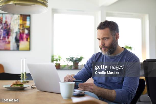 businessman paying through credit card on laptop at home - mann mit kreditkarte stock-fotos und bilder