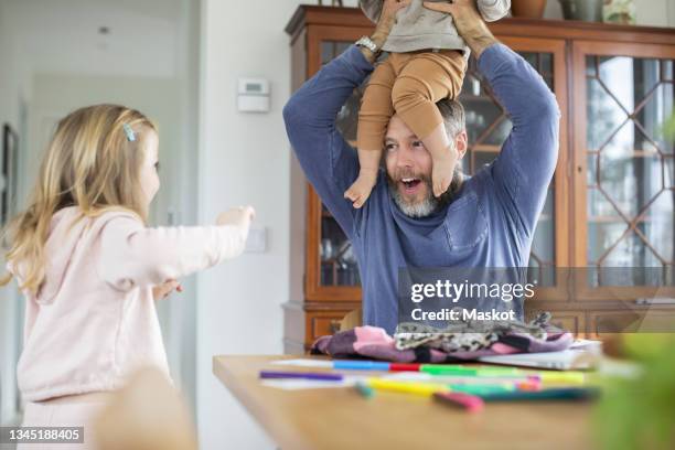 cheerful father carrying son on head while playing with daughter at home - portare sulla testa foto e immagini stock