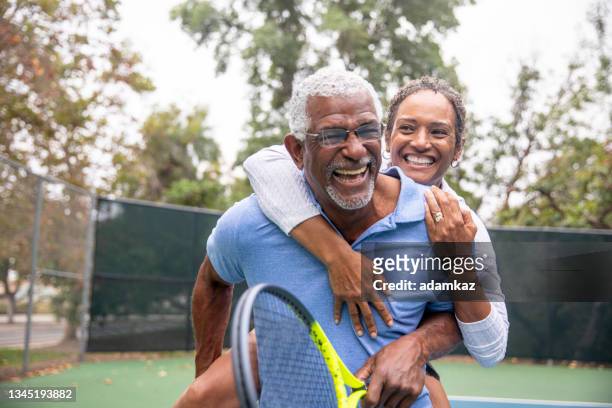 senior black couple on tennis court piggyback - fitness couple stockfoto's en -beelden