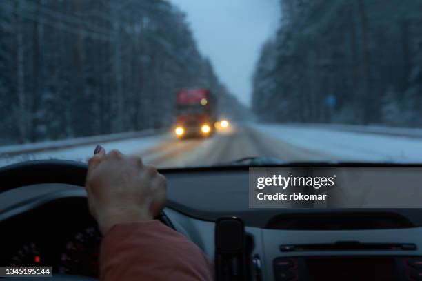 driving a car at night with headlights on along a forest snowy highway - schneeregen stock-fotos und bilder