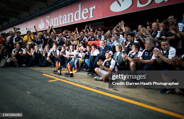 Smiling, and clapping, Williams Formula One Team mechanics, engineers, catering, and marketing staff raise their arms and clench their fists with...