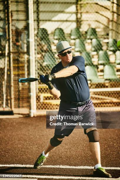 wide shot of senior softball player swinging at pitch during game on summer morning - baseball swing stock pictures, royalty-free photos & images