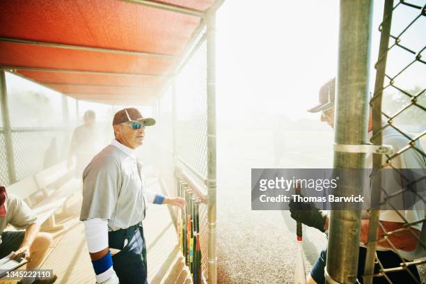 wide shot of mature softball player greeting teammate in dugout during game on summer morning - dugout baseball stock pictures, royalty-free photos & images