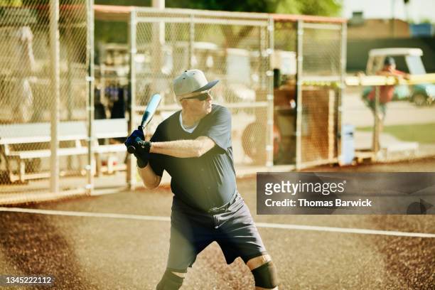 Medium wide shot of senior softball player preparing to swing during at bat during game on summer morning