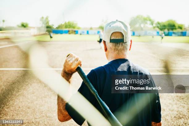 Medium shot rear view of senior softball player waiting to bat during game on summer morning