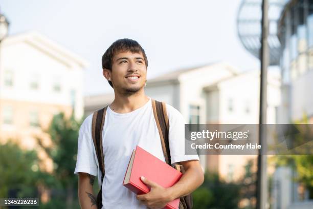 college student walking campus while holding book - community college campus stock pictures, royalty-free photos & images