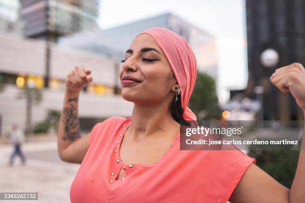 pretty with pink cancer scarf woman with raised arms showing muscle - tumor stockfoto's en -beelden