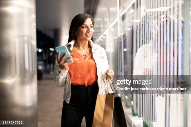 pretty south american woman with shopping bags looking at her smartphone, black friday - black friday shopping - fotografias e filmes do acervo