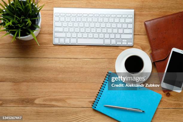 a mobile phone, a computer keyboard, a pen and notepad for notes, a coffee mug and a flower on a wooden table. subjects of work of a businessman or manager in the workplace. - mobile device on table stockfoto's en -beelden