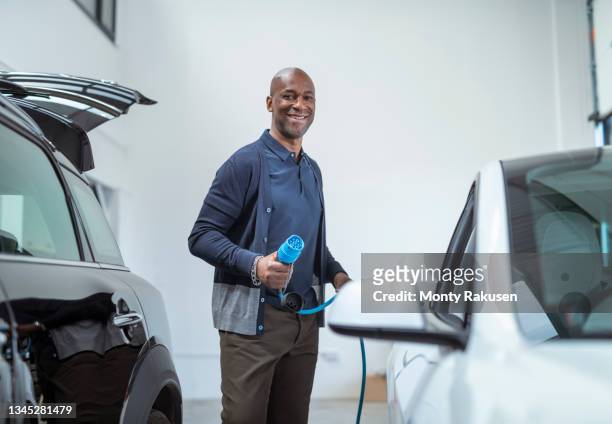 uk, portrait of smiling man holding electric plug at electric car - tesla interior stock pictures, royalty-free photos & images