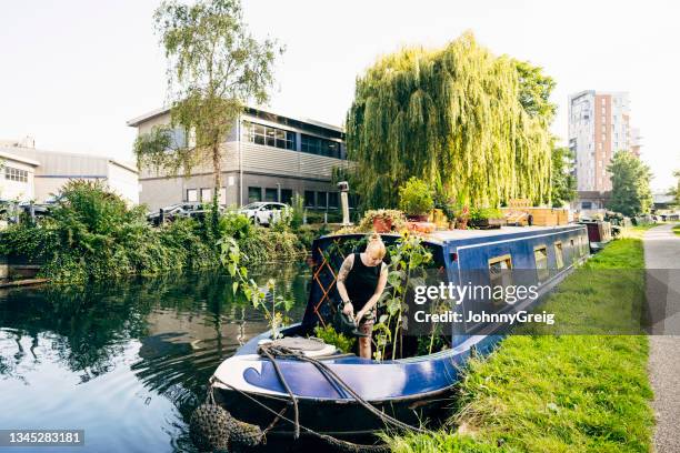 woman in late 30s watering plants on canal boat - house boat stock pictures, royalty-free photos & images