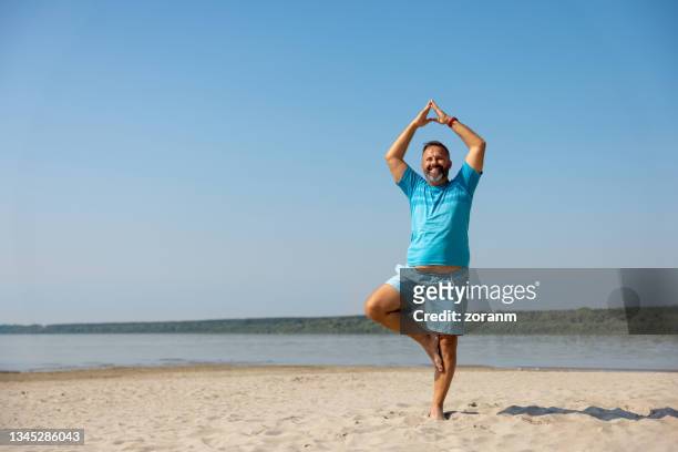 hombre feliz haciendo yoga en pose de árbol en la playa en un día despejado - fat guy on beach fotografías e imágenes de stock