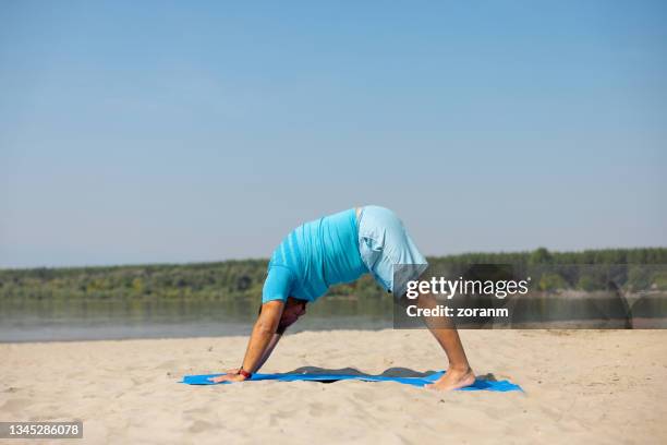 man practicing yoga on the beach in downward facing dog pose - fat man on beach stockfoto's en -beelden