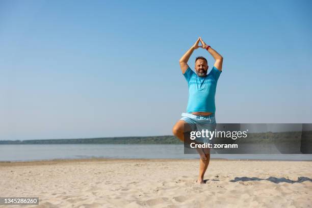 mann, der an einem klaren tag yoga in baumpose am strand praktiziert - beach yoga stock-fotos und bilder