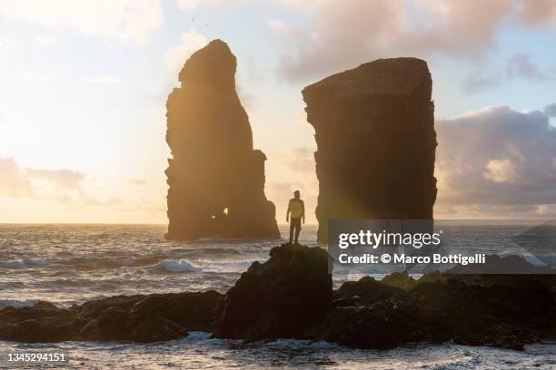 person standing on a rock among giant sea stacks - azores people stock pictures, royalty-free photos & images