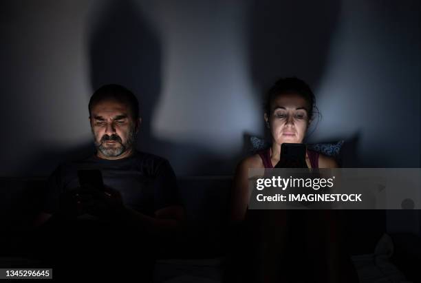 couple using their mobile phones on the sofa at home at night - vício imagens e fotografias de stock