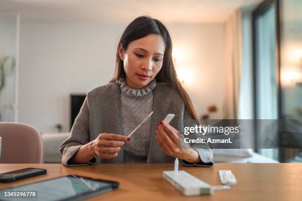 asian woman holding covid rapid test and waiting for results - corona stockfoto's en -beelden