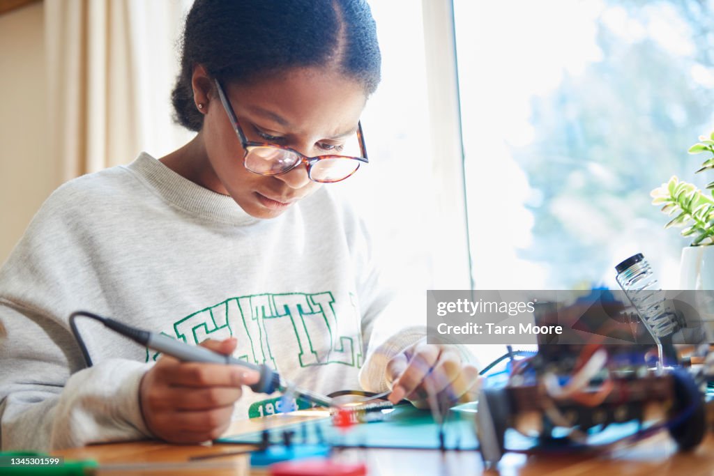 Teenage girl building robot with soldering iron
