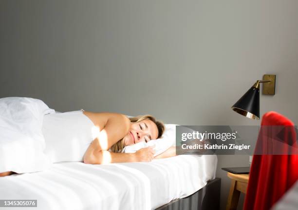 woman waking up happy in cozy hotel bed - white bed cushion stock-fotos und bilder