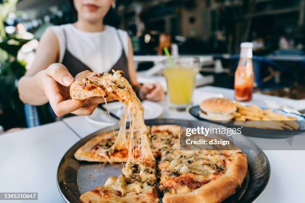 close up of young asian woman getting a slice of freshly made cheesy seafood pizza, enjoying her lunch in an outdoor restaurant. eating out lifestyle - carbohidrato fotografías e imágenes de stock