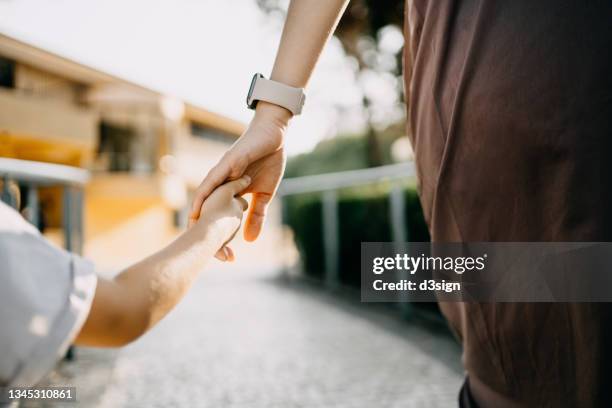 rear view, close up of young asian mother walking hand in hand with her little daughter, enjoying family bonding time in park along a footpath at sunset. family love and care - holding hands close up stock-fotos und bilder