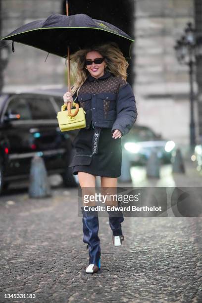 Emili Sindlev wears a black umbrella from Le Bristol, black sunglasses, gold earrings, a black fabric and brown LV monogram in coated canvas yoke...