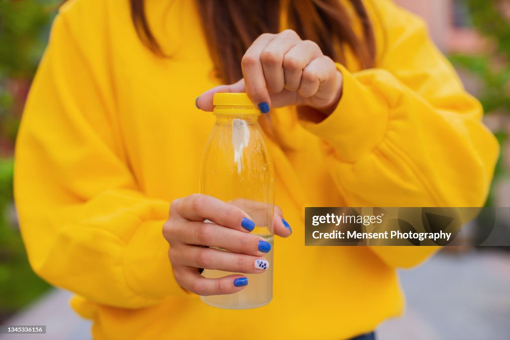Close-up of a woman opening a bottle of lemon juice standing on the street