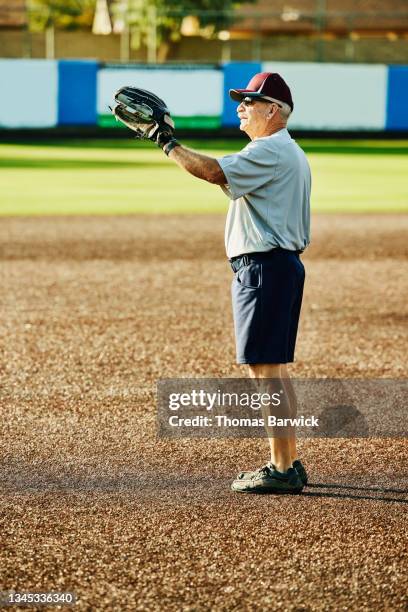 wide shot of senior softball player standing on field warming up for game on summer morning - softball sport stock pictures, royalty-free photos & images