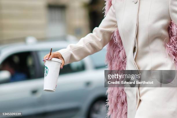 Close-up view of a white long jacket worn as a mini dress with an attached pink fluffy winter long cape, an a Starbucks Coffee cup, outside Lanvin ,...
