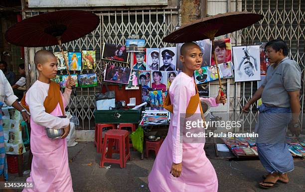 Burmese nuns walk past a street vendor's stall displaying posters of human rights activist and politician Aung San Suu Kyi and her father Aung San on...