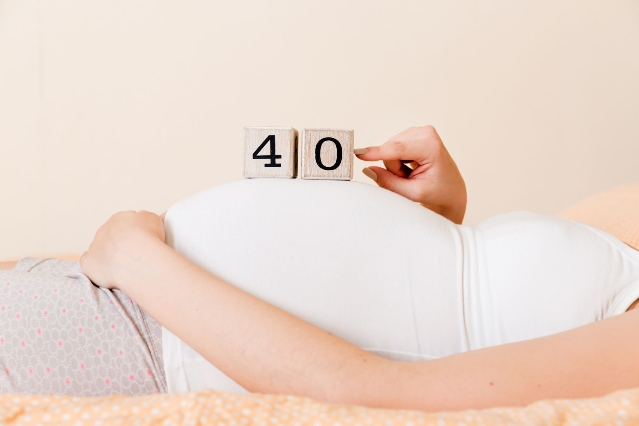 Pregnant woman in white underwear on bed in home holding calendar with weeks 40 of pregnant. Maternity concept. Expecting an upcoming baby Pregnant woman in white underwear on bed in home holding calendar with weeks 40 of pregnant. Maternity concept. Expecting an upcoming baby