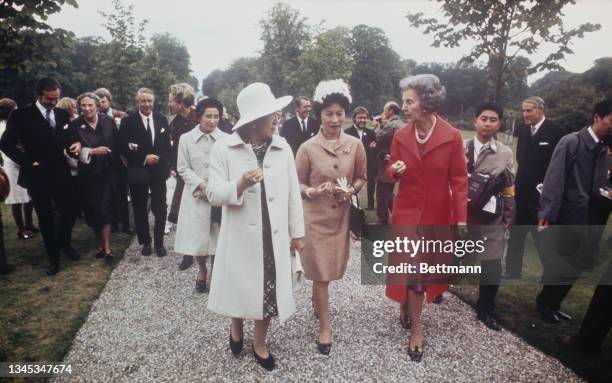 Empress Kojun of Japan chats with Queen Ingrid of Denmark in the garden of the Danish royal country home; In the center is Mrs. Ogawa, wife of the...