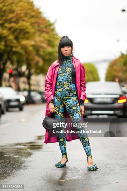 Susanna Lau wears a pink shiny vinyl long trench coat, a blue and yellow floral print jumpsuit with integrated stirrup leggings, a black Lanvin...