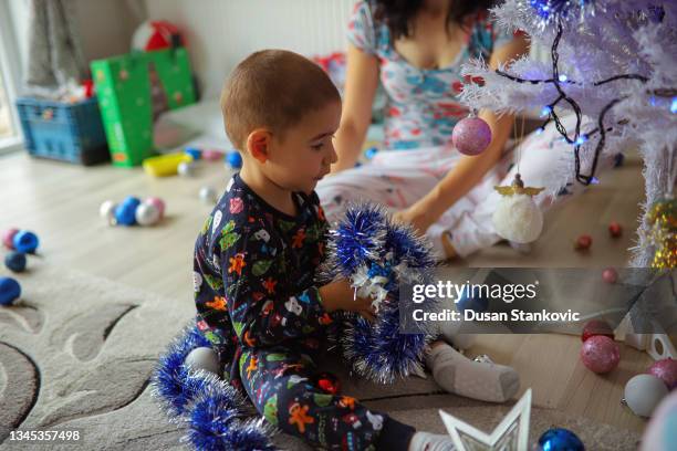 encantador niño demasiadodler, jugando con oropel, mientras con su madre decora el árbol de navidad - toodler fotografías e imágenes de stock