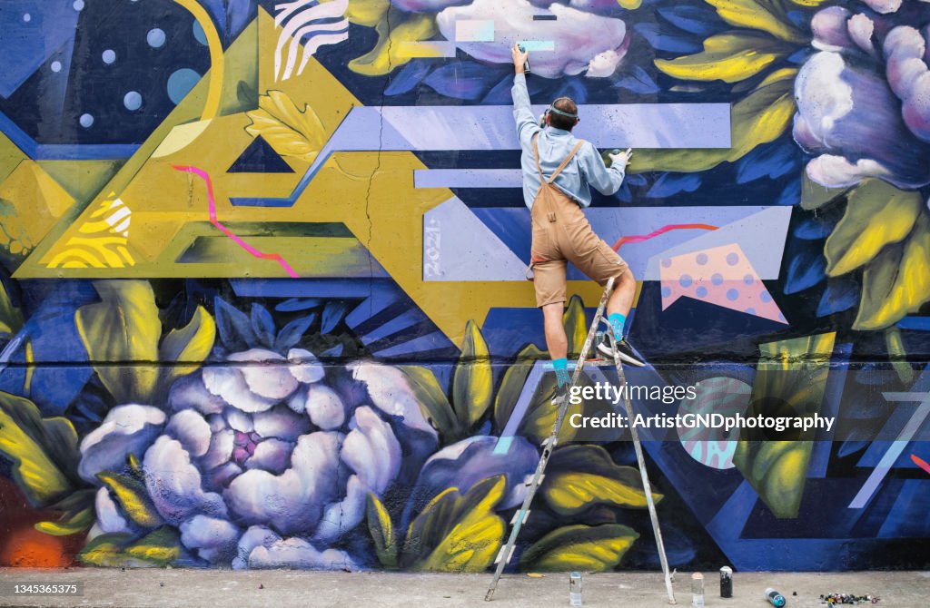 Artista di strada su una scala che disegna sul muro