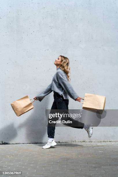 woman walking along street with two shopping bags - purchase stock-fotos und bilder