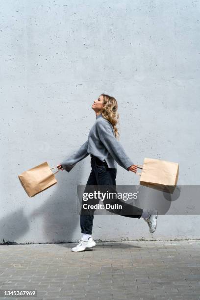woman walking along street with two shopping bags - shopping bag stock pictures, royalty-free photos & images