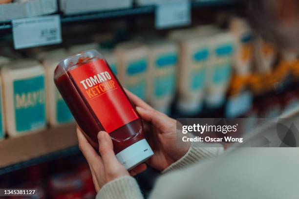 close-up of young woman doing grocery shopping in supermarket, holding a bottle of ketchup - tomato sauce stock pictures, royalty-free photos & images