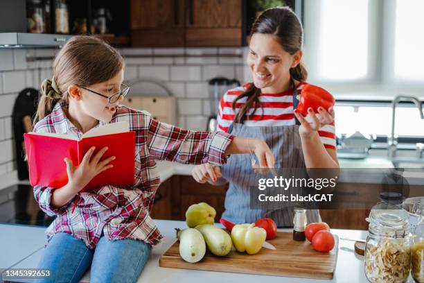 daughter helps her mother in the kitchen and reads a recipe - baking reading recipe stockfoto's en -beelden