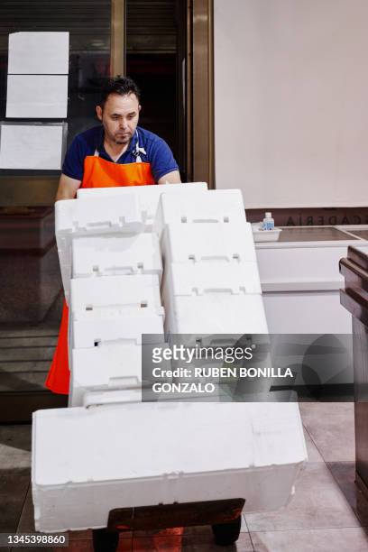 fishmonger wearing orange apron carrying a push cart with white polystyrene boxes of fresh fish on ice at a fish market for selling. small business concept. - gonzalo caballero fotografías e imágenes de stock