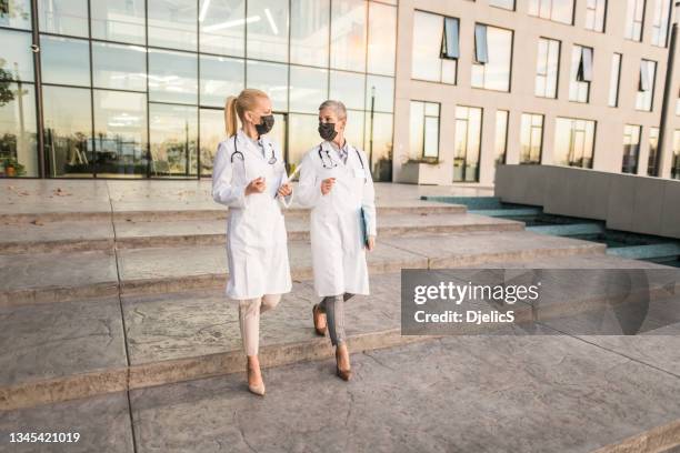 two female doctors walking in front of hospital and communicating. - nurse leaving stock pictures, royalty-free photos & images