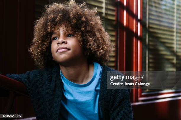 latin boy, with afro hair, looking away, with a pensive and dreamy expression. with a street in the background. children, latins, integration, immigration, and education concept. - dominican ethnicity stock pictures, royalty-free photos & images