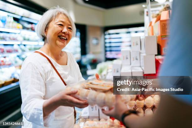 senior asian woman with young man shopping for eggs in supermarket. - senior women shopping stock pictures, royalty-free photos & images